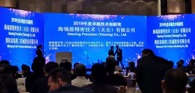 blaue Leinwand mit weißer chinesischer Schrift "2019 - Häring Precision (Taicang) Co., Ltd" vor Bühne sitzen Menschen hören sich den Vortrag an