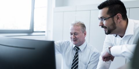Zwei männliche Mitarbeiter von Häring an einem Schreibtisch, einer steht und der andere sitzt , sie unterhalten sich