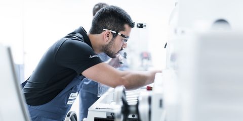 dunkelhaariger männlicher Mitarbeiter mit Brille an CNC-Maschine